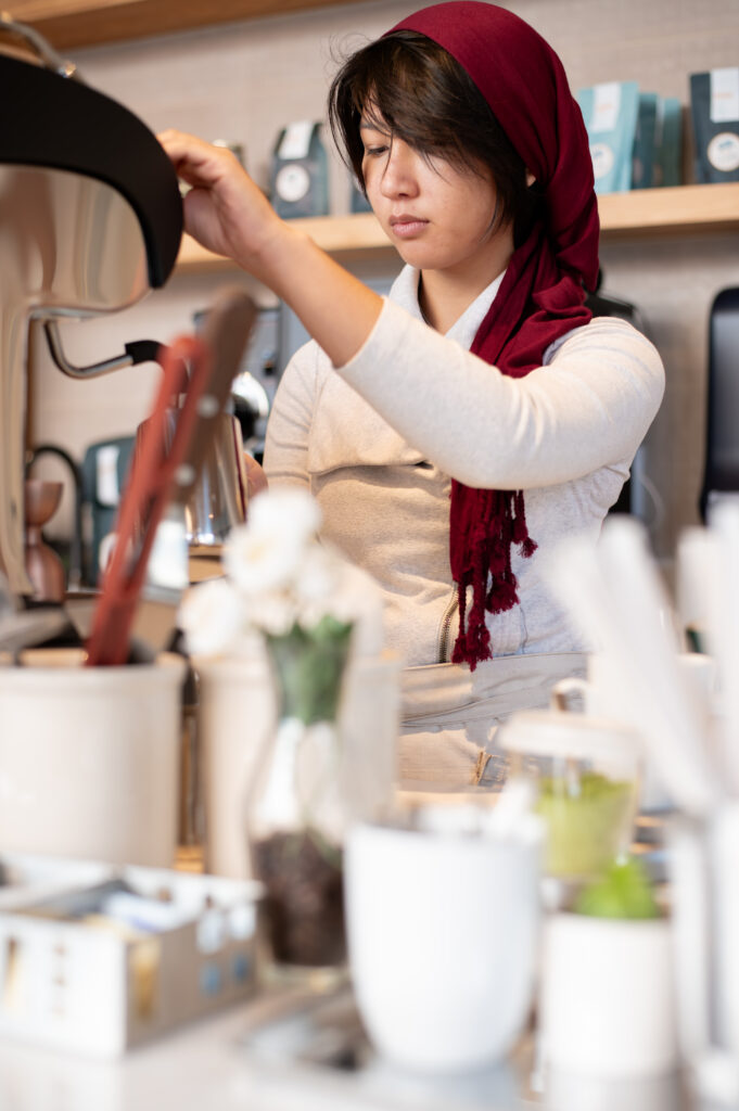 Barista wearing a red scarf and white clothing frothing up some milk.