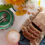 Pumpkin Spice Banana Bread on table with autumn flowers, a cafe latte and green pastry plates with silver forks.